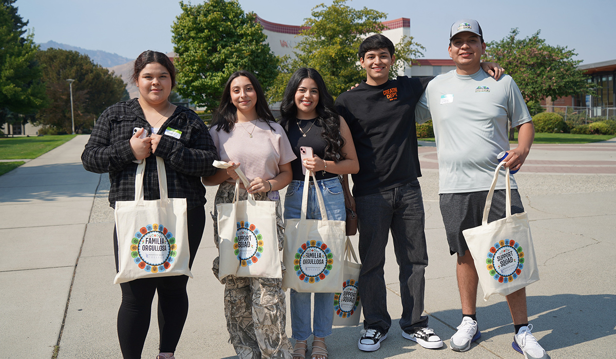 Un grupo de estudiantes posa juntos frente al Van Tassell Center con sus bolsas de orientación en la mano.