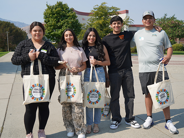 Cinco estudiantes están de pie en grupo, con las bolsas de tela que recibieron en la sesión de orientación para nuevos alumnos.