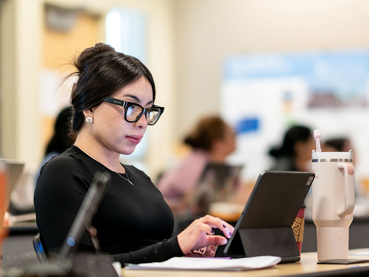 Una estudiante con gafas en clase, delante del ordenador.