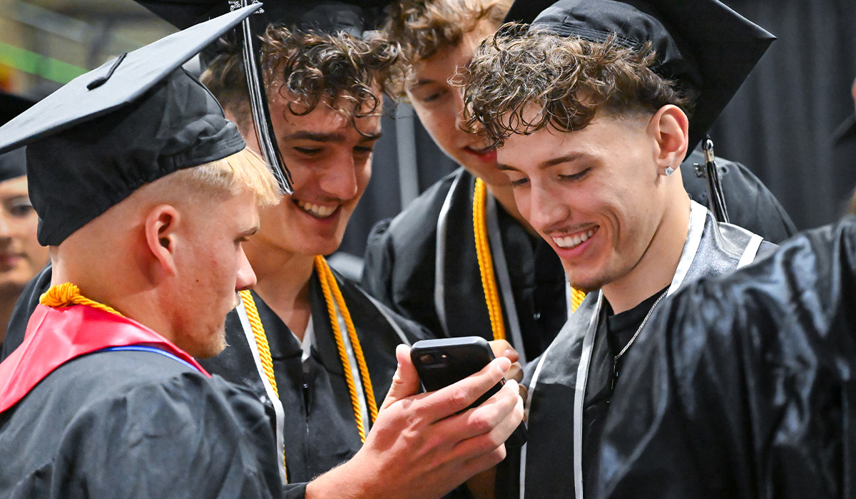 Varios graduados, ataviados con toga y birrete, miran la pantalla de un teléfono.