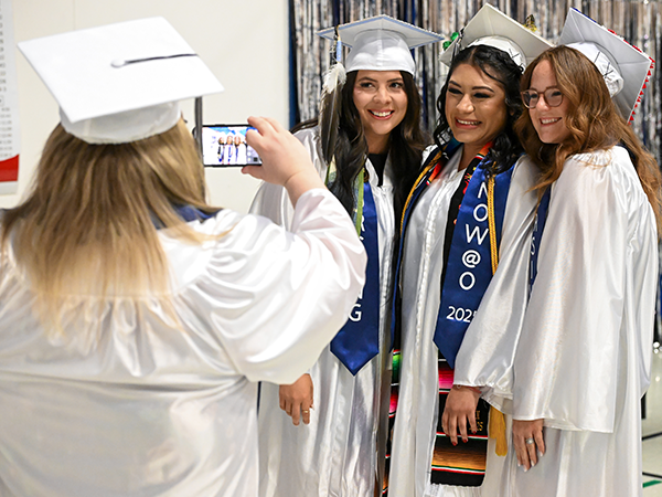 Tres graduados de WVC Omak sonríen para una foto, mientras otro graduado les hace la foto.