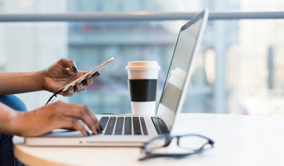 Un par de manos teclean en un ordenador portátil y sostienen un teléfono móvil.