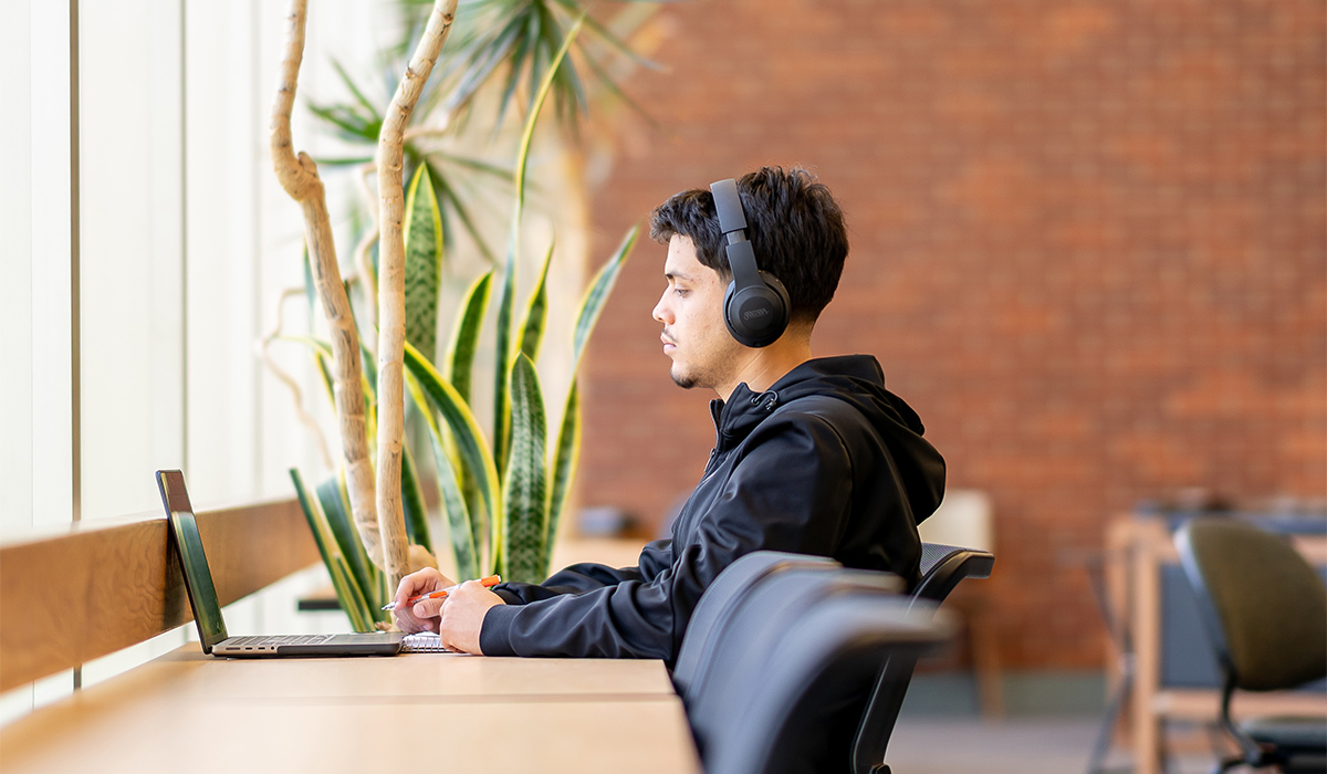 Un estudiante está sentado en una mesa larga y trabaja con un ordenador portátil.