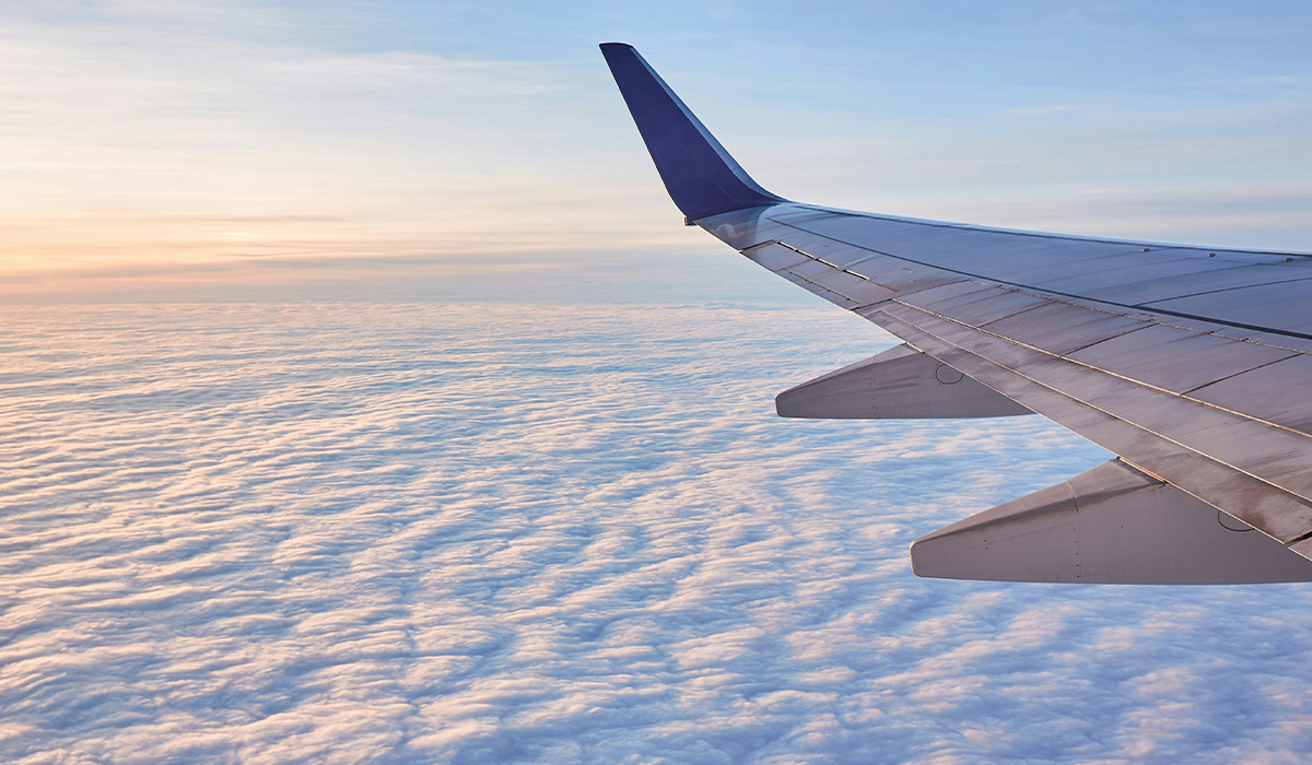 Una vista desde la ventanilla de un avión en la que se ven el ala del avión, las nubes y el cielo azul.