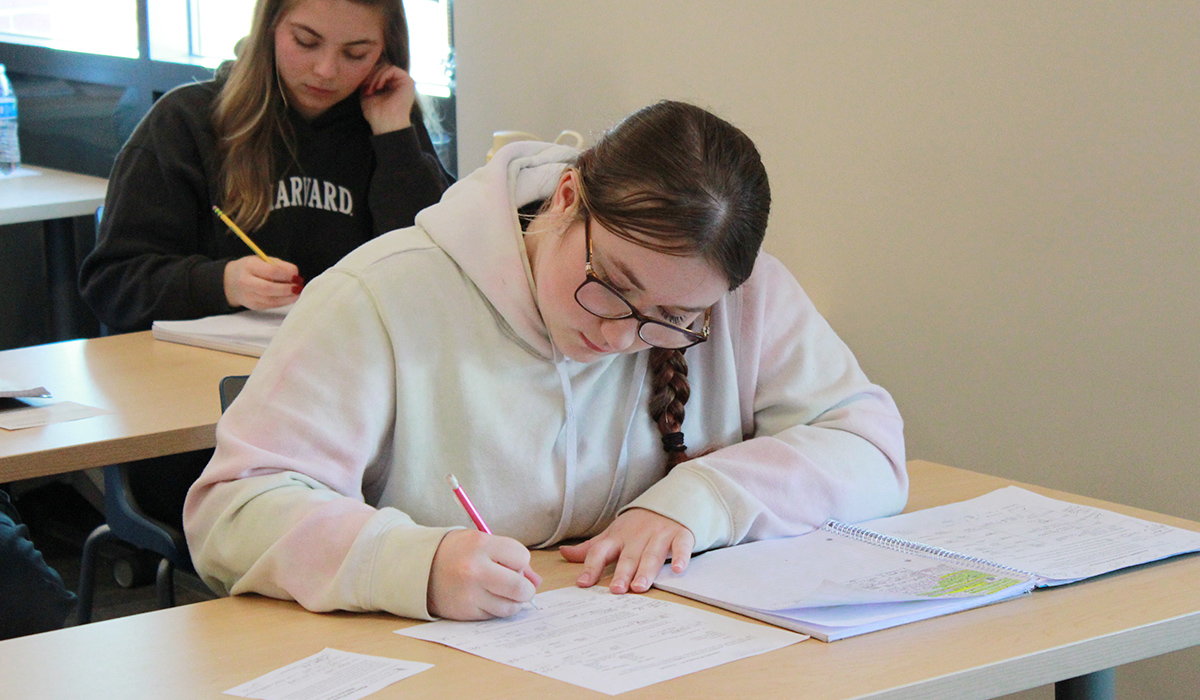 Un estudiante escribe en una hoja de trabajo de contabilidad.