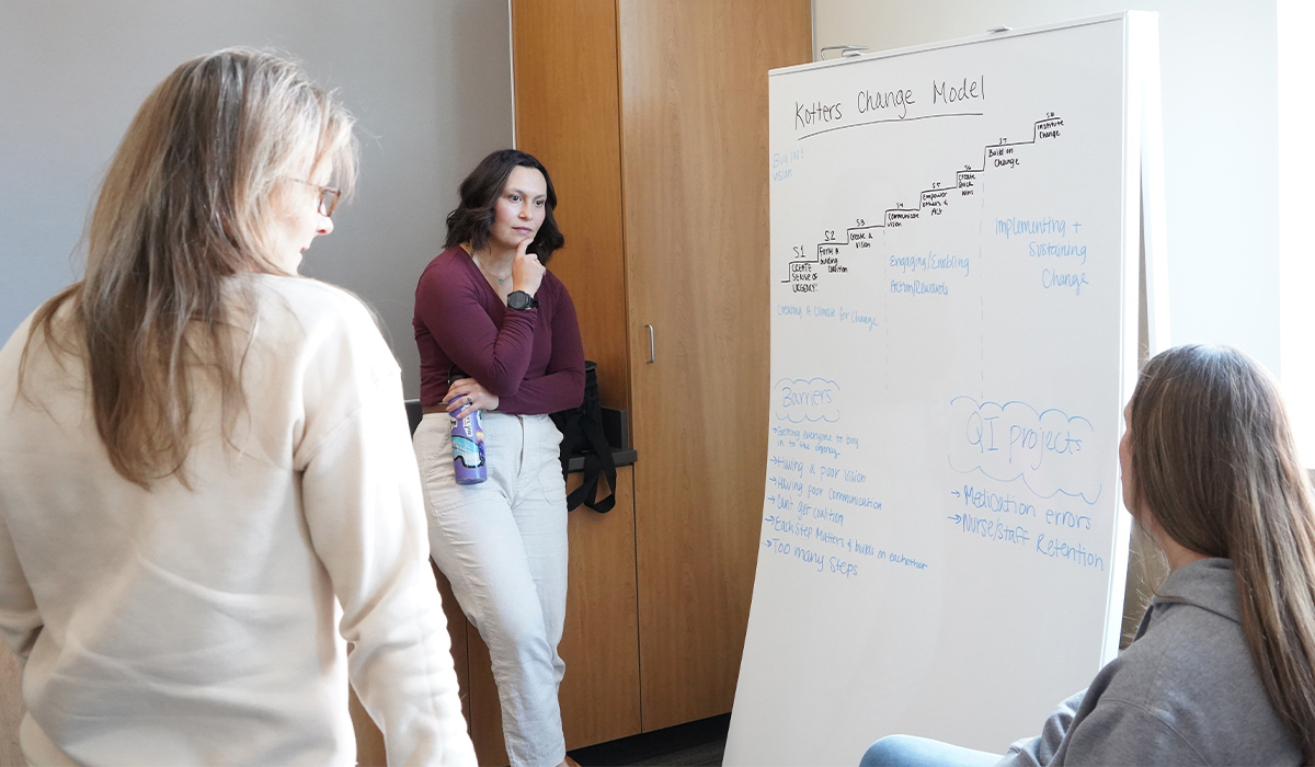 Dos estudiantes del programa de transición de enfermería (RN a BSN) hablan con su profesor sobre un proyecto en grupo.