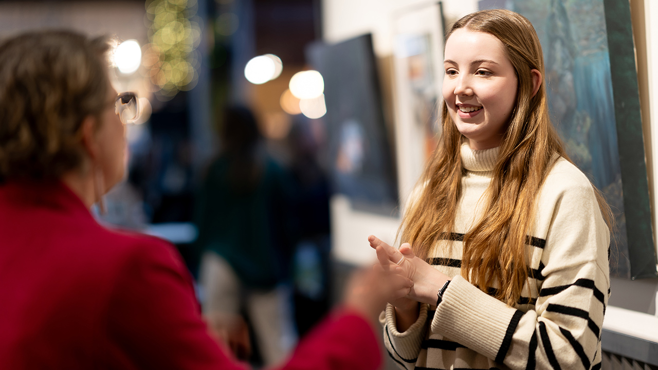 Un estudiante de Bellas Artes conversa con una persona en una exposición de arte estudiantil en Pybus Market.