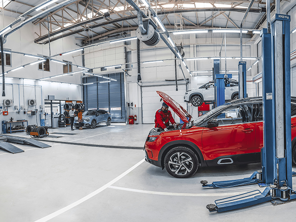 El interior de un taller mecánico, donde un mecánico está trabajando en el motor de un coche rojo.