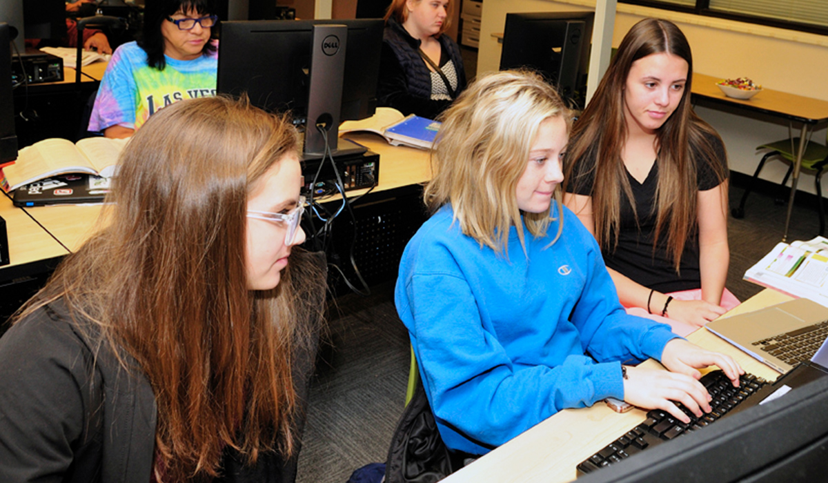 Tres estudiantes del curso de Tecnología Informática Empresarial trabajan juntos en un proyecto informático.