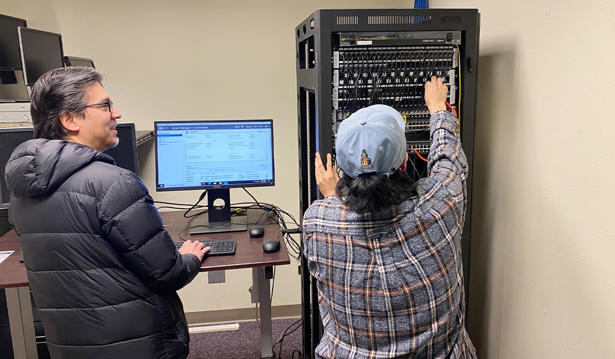 Un alumno trabaja en una red informática mientras el profesor observa.