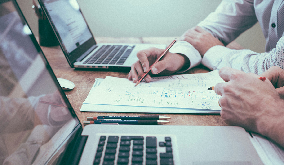 Dos personas están sentadas a una mesa con sus ordenadores portátiles y revisan un diseño.