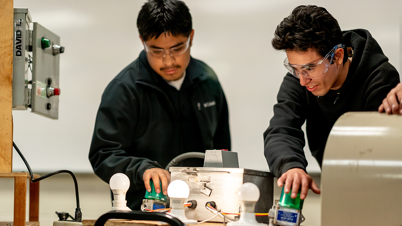Dos estudiantes hacen una demostración de un proyecto de electrónica que enciende bombillas.