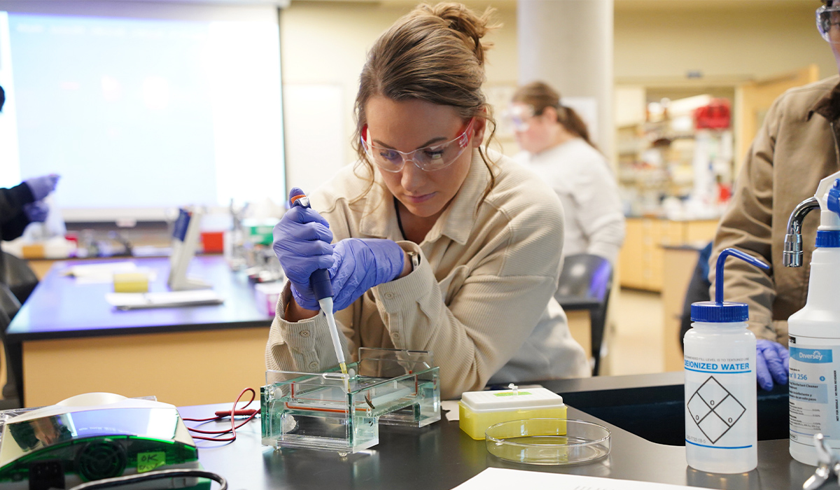 Un estudiante de la Universidad de Biología , ataviado con una bata de laboratorio y gafas protectoras, realiza un experimento en un laboratorio.