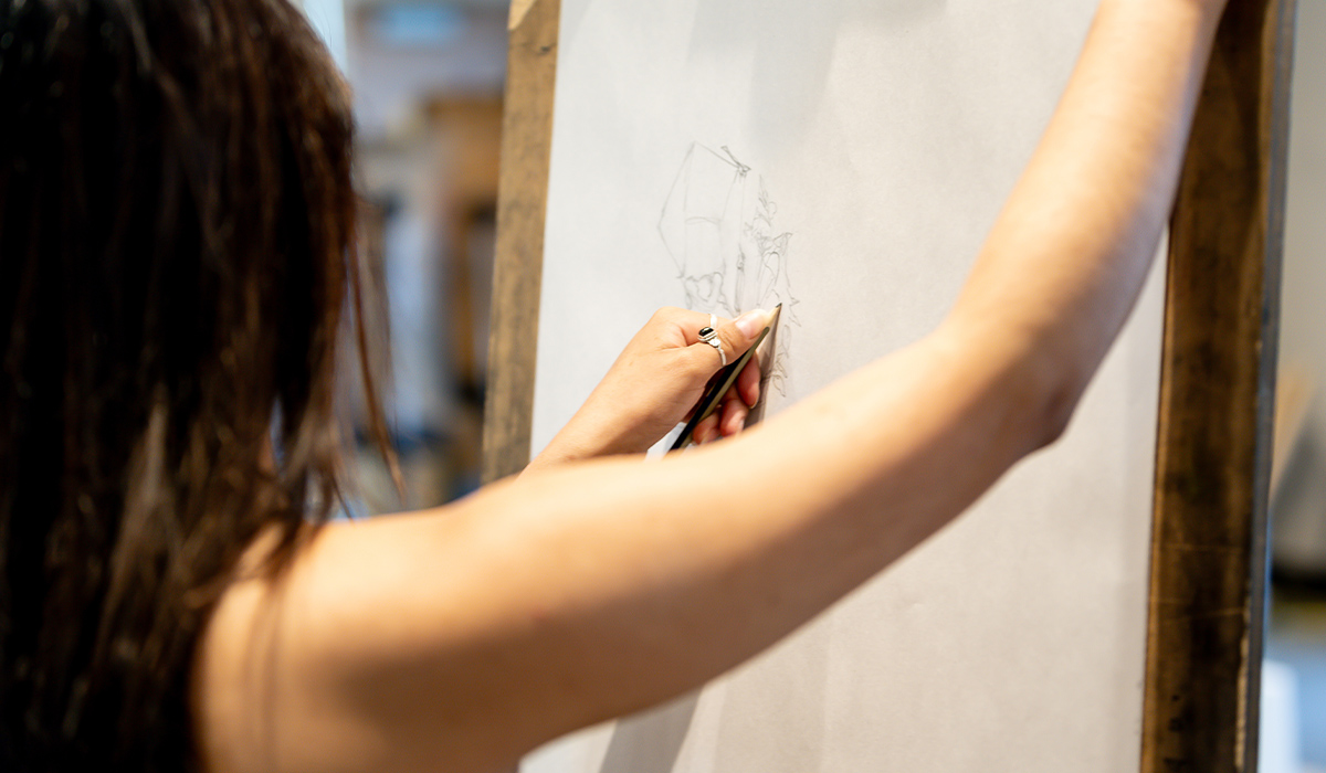Un estudiante de Bellas Artes se encuentra de pie frente a un caballete y está realizando un boceto.