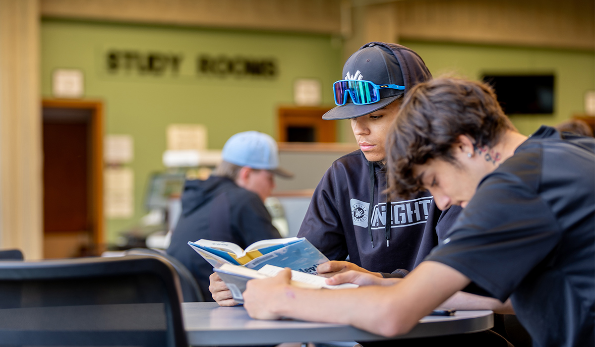 Dos estudiantes están sentados en una mesa de la biblioteca y leen libros.