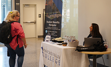 Magali Olguín-Ramos está sentada a una mesa y habla con un estudiante que pasa por allí.