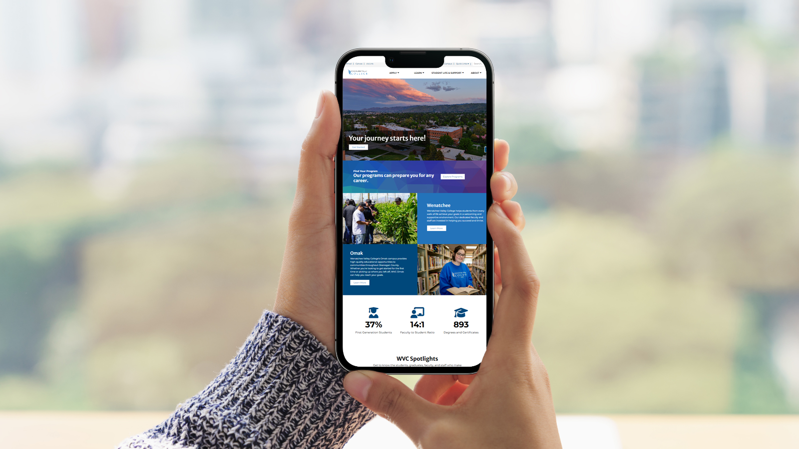 Un par de manos sostienen un teléfono móvil en cuya pantalla se ve la página web de WVC.