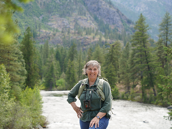 Heather Wallis Murphy aparece en primer plano, con un río, un bosque y unas montañas a sus espaldas.