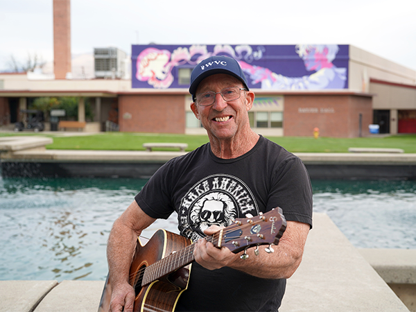 Tom Martin se encuentra junto a la fuente de « campus » de Wenatchee, con su guitarra en la mano.