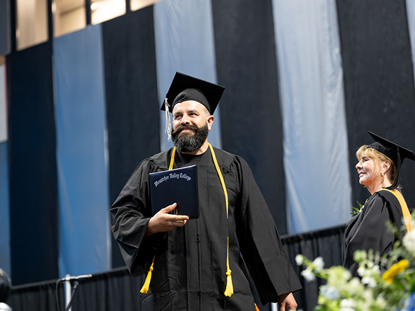 Un graduado cruza el escenario con su título en la mano.
