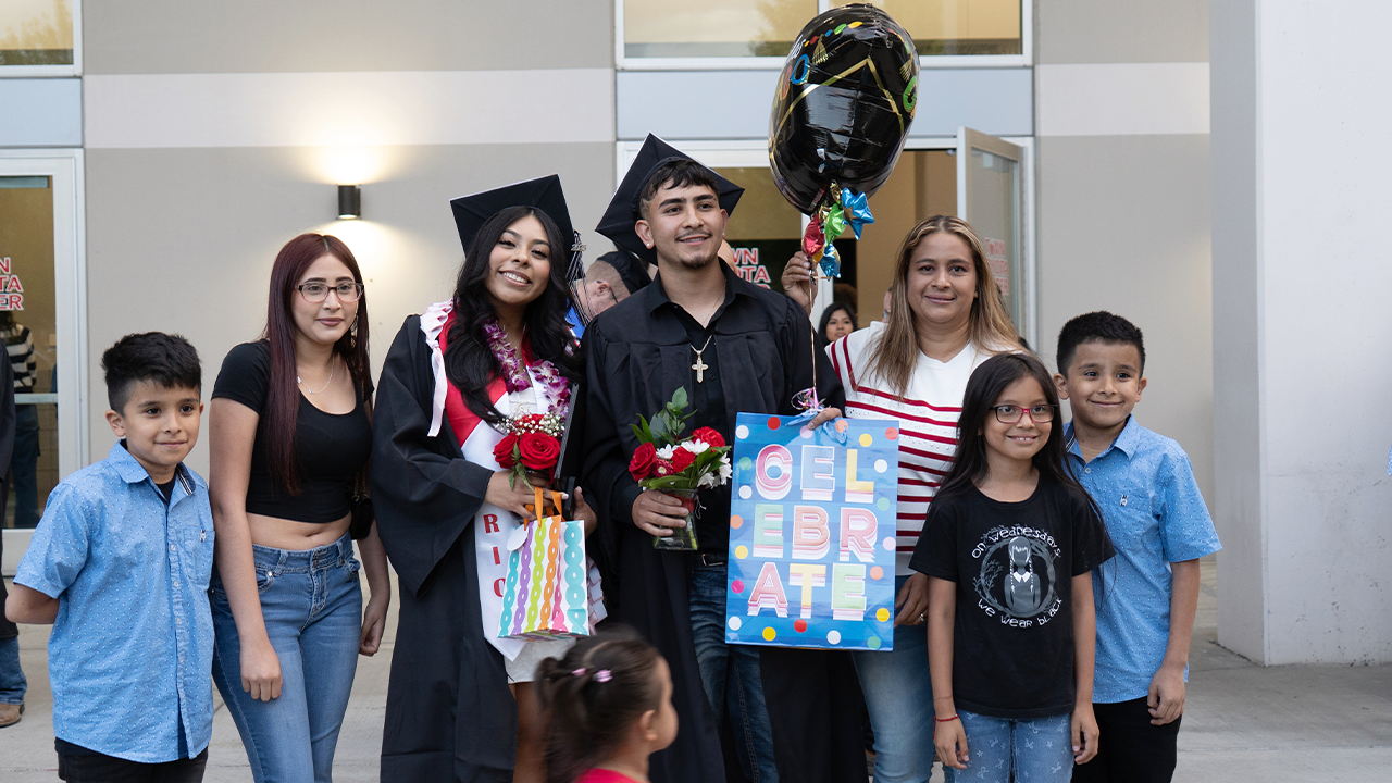 Dos graduados posan junto a sus familiares con flores y globos en la mano tras la ceremonia de graduación.