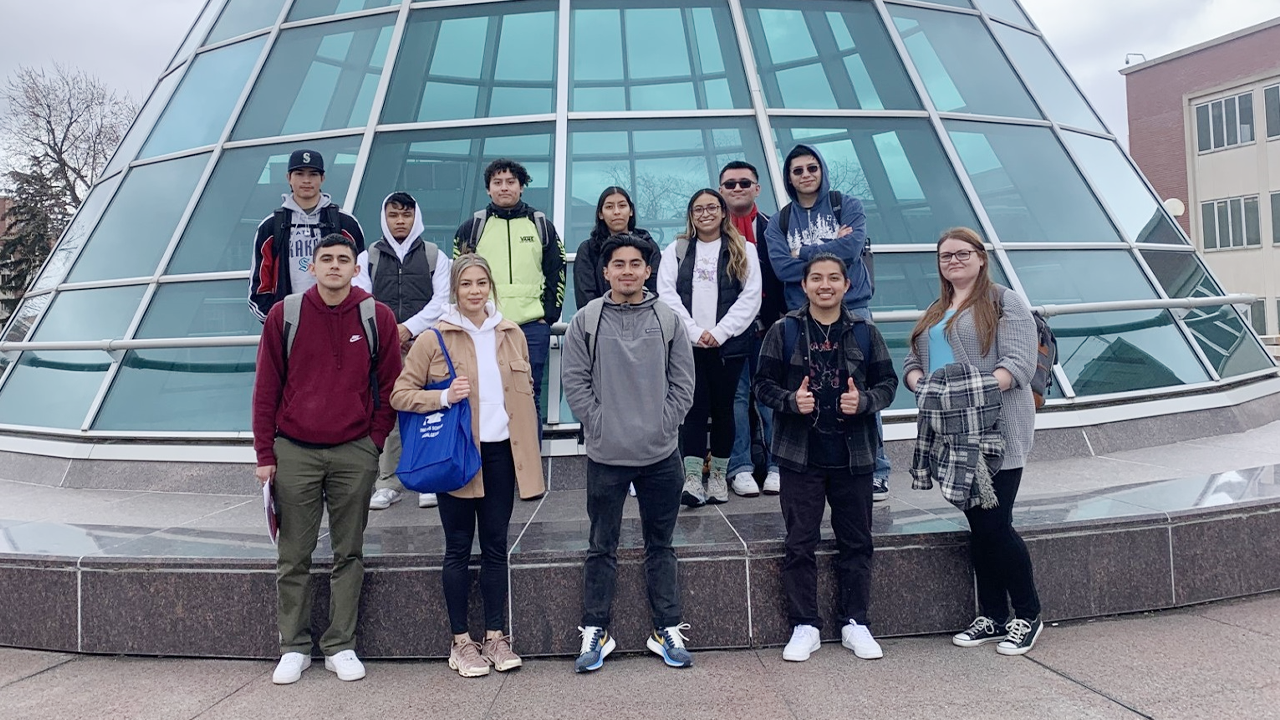 Un grupo de estudiantes del programa TRIO posa junto a una estructura de cristal.